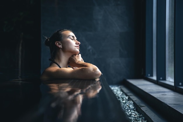 Attraktive junge Frau in einem schwarzen Badeanzug entspannt sich im Pool