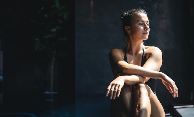 Attraktive junge Frau in einem schwarzen Badeanzug entspannt sich im Pool