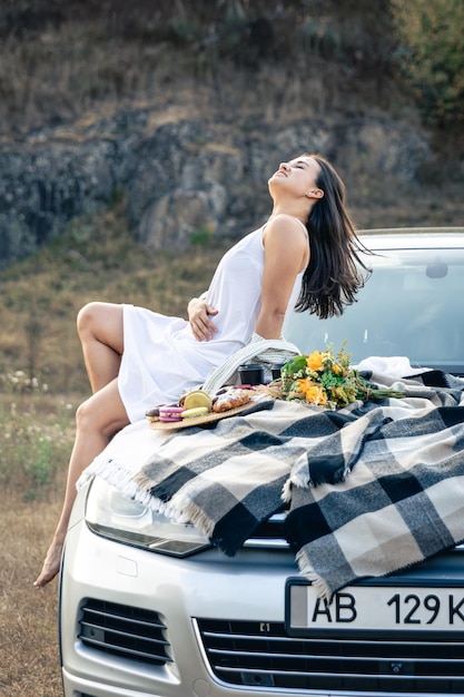 Kostenloses Foto attraktive junge frau liegt auf der motorhaube des autos und blickt auf den sonnenuntergang