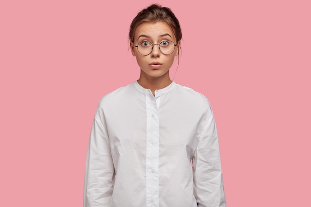 attraktive junge Frau mit Brille, die gegen die rosa Wand aufwirft