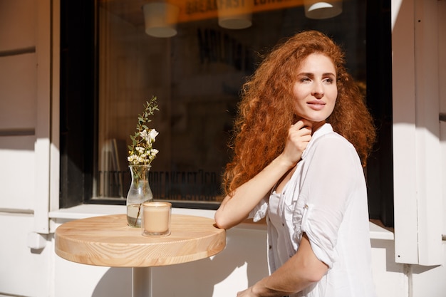 Attraktive junge Frau mit dem lockigen Haar, das am Tisch sitzt