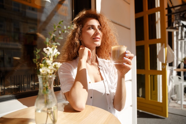 Attraktive junge Frau mit dem lockigen Haar, das am Tisch sitzt