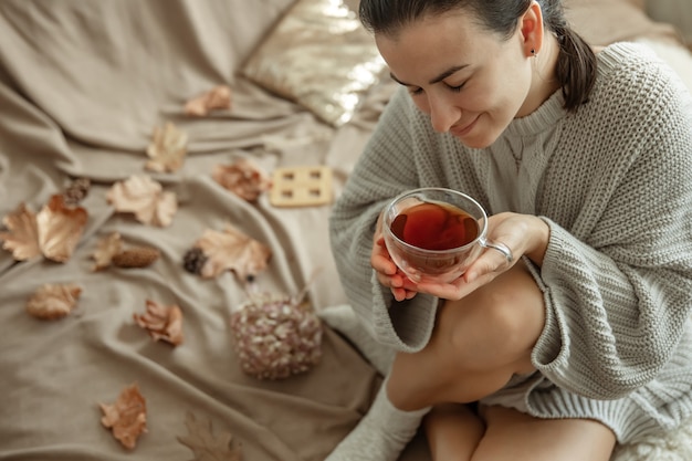 Attraktive junge Frau trinkt Tee, der im Bett zwischen den Herbstblättern sitzt