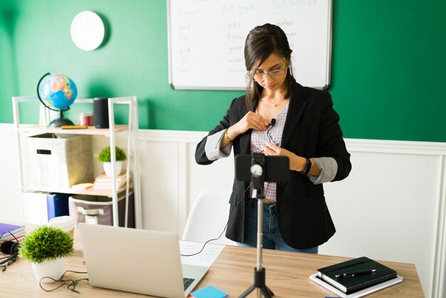 Attraktive junge Lehrerin, die ihr Mikrofon aufsetzt, um von zu Hause aus einen virtuellen Highschool-Unterricht zu geben