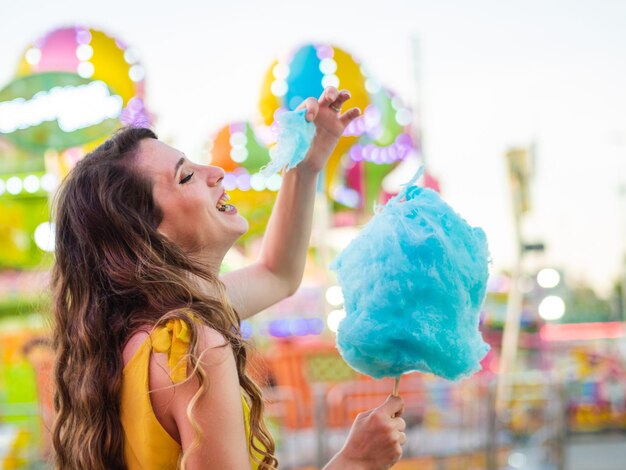 Attraktive kaukasische Frau, die bei einem Karneval mit blauer Zuckerwatte posiert