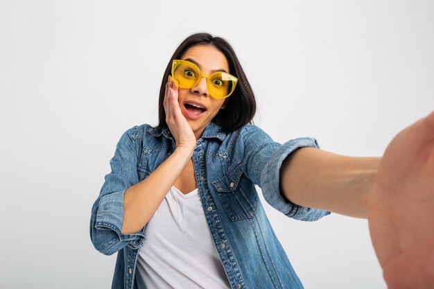 Attraktive lächelnde aufgeregte Frau, die Selfie-Foto mit überraschtem Gesicht lokalisiert auf Weiß macht