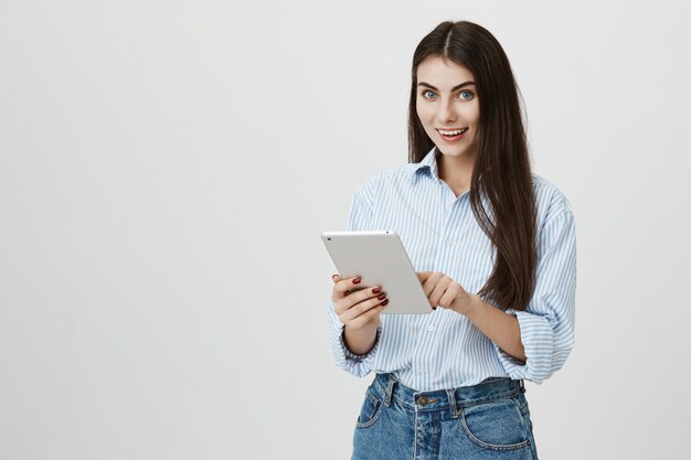 Attraktive lächelnde Frau, die digitales Tablett bei der Arbeit verwendet
