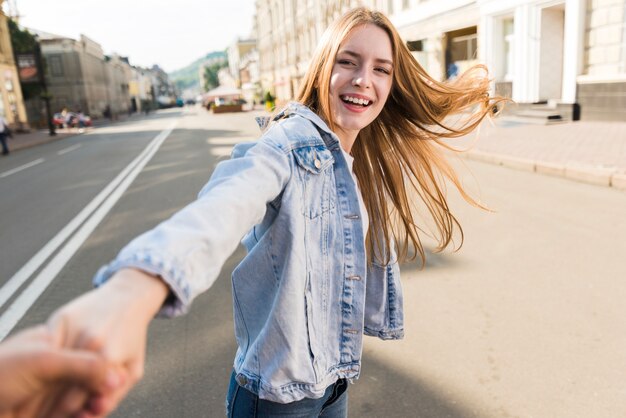 Attraktive lächelnde junge Frau, welche die Hand ihres Freundes auf Straße führt