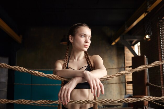 Attraktive muskulöse junge Frau, die drinnen im Boxring aufwirft, Ruhe nach intensivem Training hat