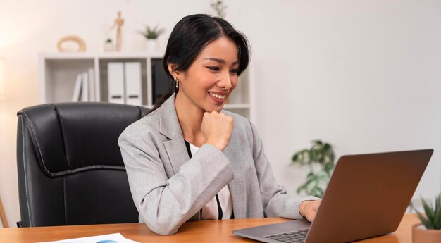 Attraktive, reife Geschäftsfrau des schönen asiatischen Managers, die an ihrem Arbeitsplatz am Laptop arbeitet