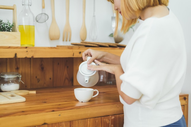 Attraktive schöne asiatische Frau, die warmen Kaffee in der Küche an ihrem Haus genießt