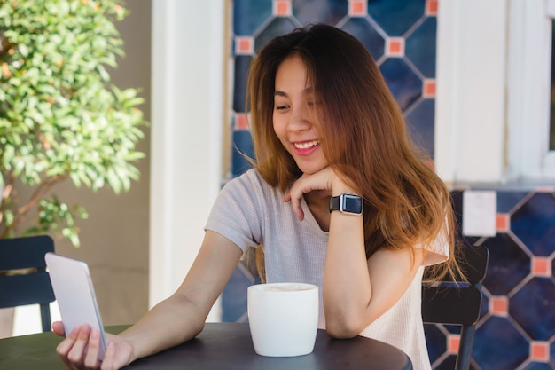 Attraktive schöne glückliche junge Asiatin, die ein selfie unter Verwendung eines intelligenten Telefons am Café nimmt