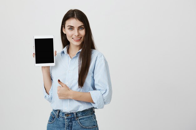 Attraktive selbstbewusste Frau Daumen hoch als Anzeige digitaler Tablet-Bildschirm