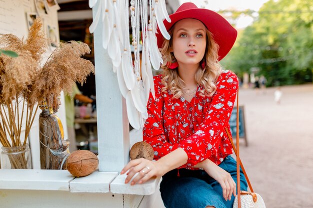 Attraktive stilvolle blonde lächelnde Frau im strohroten Hut und im Sommermode-Outfit-Café der Bluse