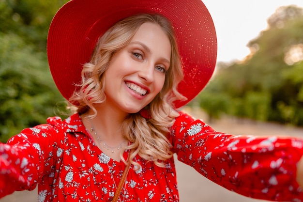 Attraktive stilvolle blonde lächelnde Frau in strohrotem Hut und Bluse Sommermode-Outfit, das Selfie-Foto auf Telefonkamera nimmt