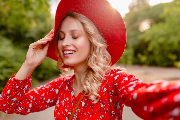 Attraktive stilvolle blonde lächelnde Frau in strohrotem Hut und Bluse Sommermode-Outfit, das Selfie-Foto macht
