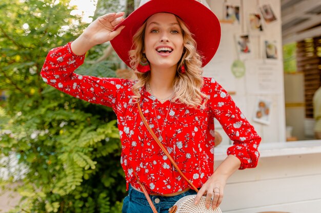 Attraktive stilvolle blonde lächelnde Frau in strohrotem Hut und Bluse Sommermode-Outfit