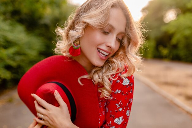 Attraktive stilvolle blonde lächelnde Frau in strohrotem Hut und Bluse Sommermode-Outfit