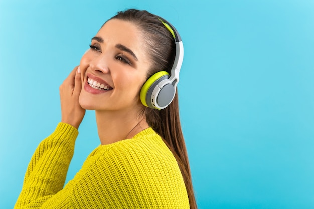 Attraktive, stilvolle junge Frau, die Musik in drahtlosen Kopfhörern hört, die gerne gelbe Strickpullover im bunten Stil trägt