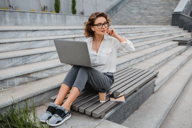 Attraktive stilvolle lächelnde Frau mit Brille, die am Laptop schreibt