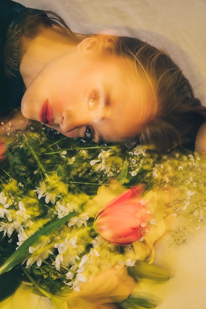 Attraktive träumerische Frau, die mit Blumenstrauß der Blumen liegt