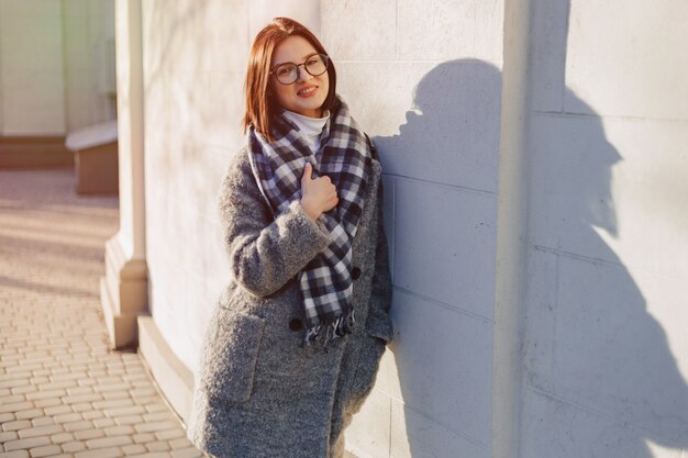 Attraktive tragende Gläser des jungen Mädchens in einem Mantel gehend an einem sonnigen Tag