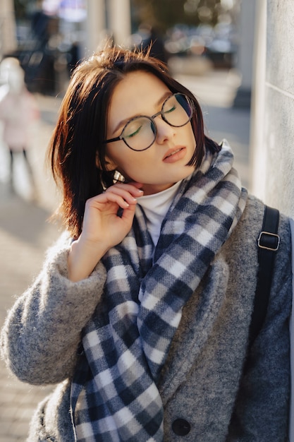 Attraktive tragende Gläser des jungen Mädchens in einem Mantel gehend an einem sonnigen Tag