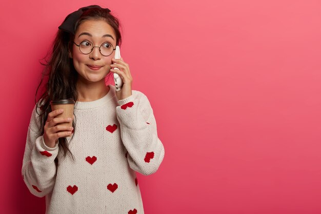 Attraktive überraschte asiatische Teenagergespräche per Handy, hört Gerüchte, trinkt Kaffee zum Mitnehmen, hat langen Pferdeschwanz