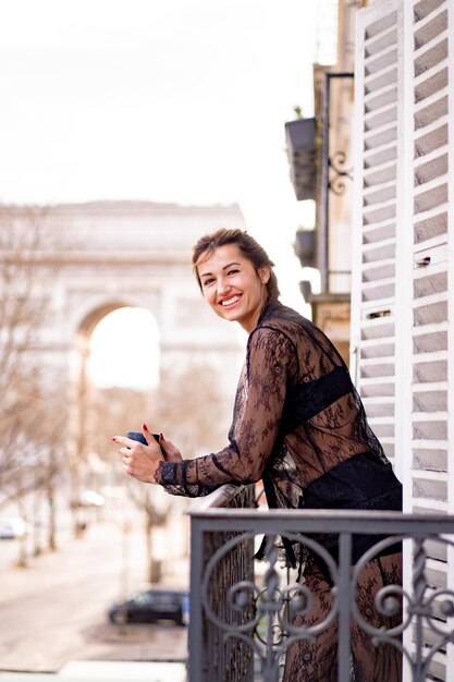 Attraktive Yang-Frau im Schlafanzug trinkt morgens Kaffee auf dem Balkon in der Stadt Paris. Blick auf den Triumphbogen.