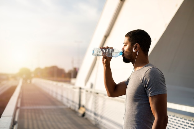 Attraktiver Athlet, der eine Flasche Wasser hält und vor dem Training trinkt