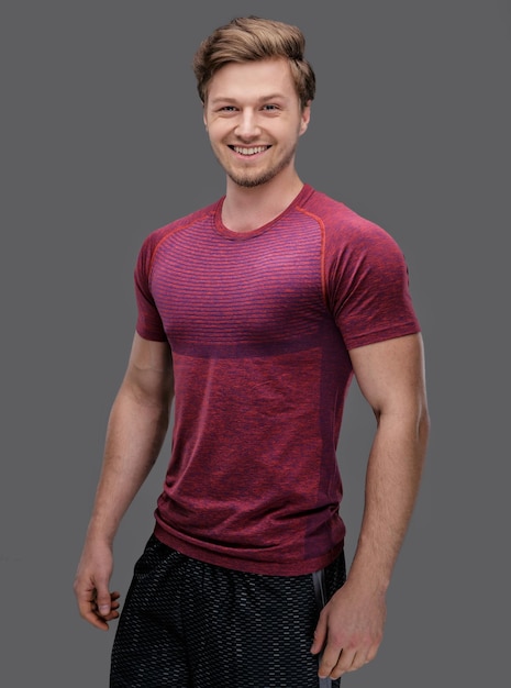 Attraktiver fitter Typ in einem roten T-Shirt isoliert auf grauem Hintergrund.