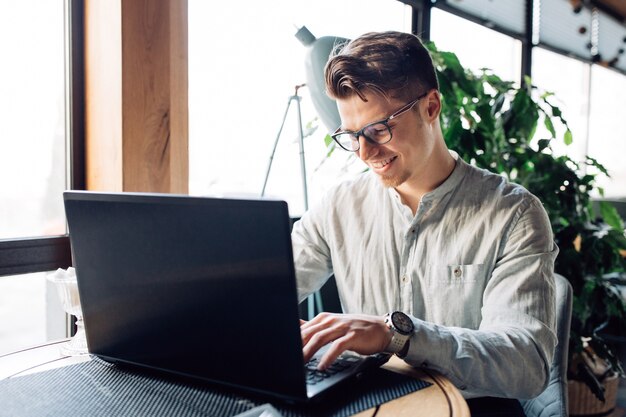 Attraktiver Geschäftsmann in den Brillen, die an Laptop arbeiten und schreiben, Zeit am Café verbringend.