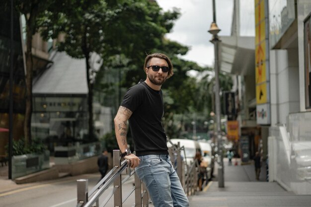 Attraktiver glücklicher tätowierter Mann, der auf der Straße in Kuala Lumpur lächelt. Urbane Männer, Kleidungsstil. Seifenblasen fliegen in die Luft.