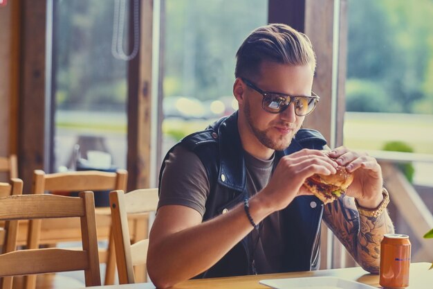 Attraktiver Hipster in Lederjacke, der einen veganen Burger isst.