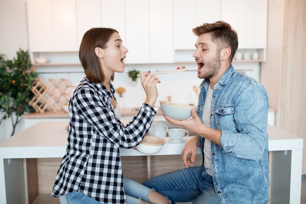 Attraktiver junger glücklicher Mann und Frau in der Küche, frühstückend, Paar zusammen am Morgen, lächelnd