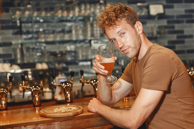 Attraktiver junger Mann, der hinter der Bar steht. Mann in einem braunen T-Shirt hält ein Glas in seinen Händen.