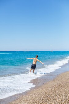 Attraktiver junger mann mit einem schönen körper in kurzen hosen geht am sandstrand entlang und genießt den sommerurlaub