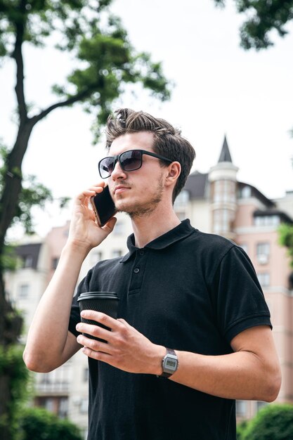 Attraktiver junger Mann mit Sonnenbrille, der auf einem Smartphone in der Stadt spricht