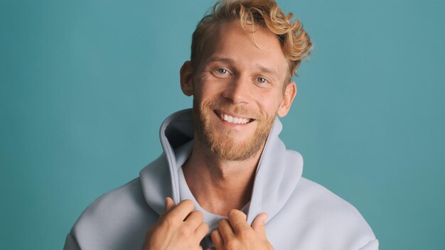 Attraktiver lächelnder blonder bärtiger Mann im Hoodie, der freudig Zeit mit Freunden verbringt, die auf blauem Hintergrund isoliert sind Gute Laune