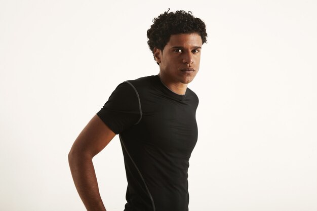 Attraktiver Mann mit einem Afro, der ein schwarzes technisches synthetisches T-Shirt mit Händen auf dem Rücken trägt