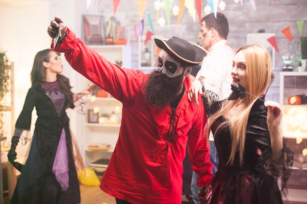 Attraktiver Mann und Frau, die wie Pirat und Vampir verkleidet sind und ein Selfie auf der Halloween-Party machen.