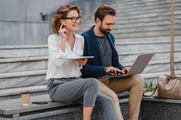 Attraktiver mann und frau sitzen auf treppen im städtischen stadtzentrum und arbeiten gemeinsam am laptop