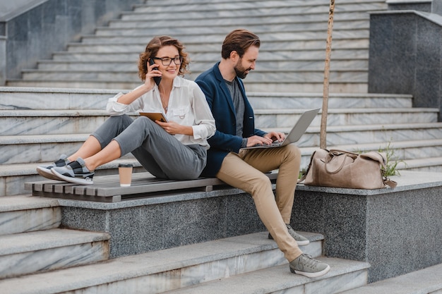 Attraktiver Mann und Frau sitzen auf Treppen im städtischen Stadtzentrum und arbeiten gemeinsam am Laptop