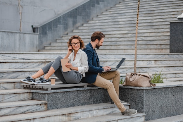 Attraktiver Mann und Frau sitzen auf Treppen im städtischen Stadtzentrum und arbeiten gemeinsam am Laptop