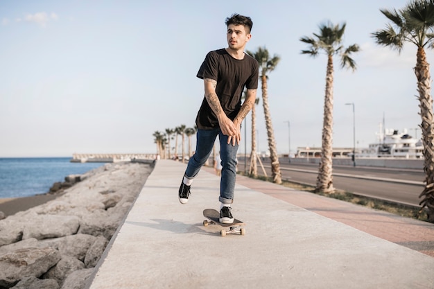 Attraktiver Teenager, der nahe der Küste Skateboard fährt