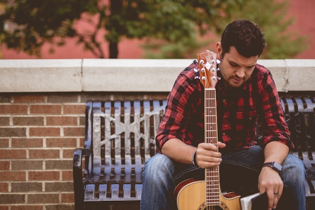 Kostenloses Foto attraktiver weißer mann, der auf einer bank sitzt, die die gitarre hält