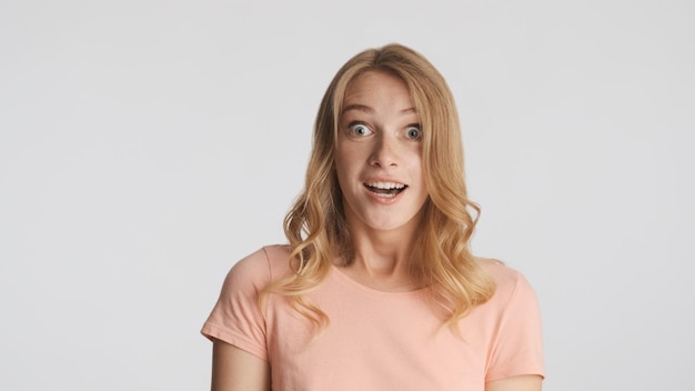 Attraktives aufgeregtes blondes Mädchen überrascht durch unerwartete Nachrichten auf Kamera lokalisiert auf weißem Hintergrund. Wow Gesicht
