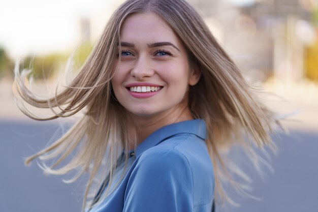 Attraktives fröhliches blondes Mädchen mit fliegenden langen Haaren, die lachend in der Stadt lächeln