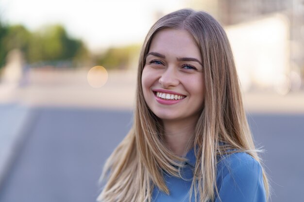 Attraktives fröhliches blondes Mädchen mit fliegenden langen Haaren, die lachend in der Stadt lächeln