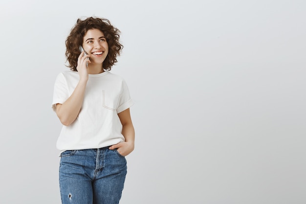 Attraktives glückliches Mädchen, das am Telefon spricht und lächelt